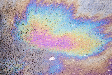 A patch of spilt oil has mixed with rain  to show iridescent rainbow colours on  a road surface