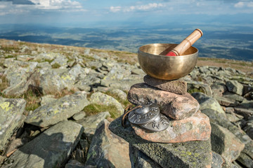 A Himalayan singing bowl placed on stones on a top of a mountain with a view over a deep valley and...