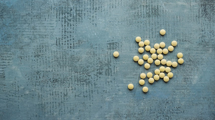 yellow round tablets or pills vitamins flat lay on blue stone concrete table, top down view, horizontal stock photo image still life background with copy space