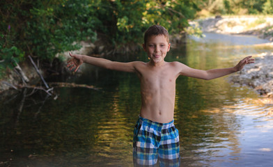A teenage boy in shorts plays in a mountain river in shallow water