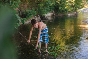 A teenage boy in shorts plays in a mountain river in shallow water