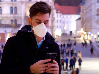Worried man wearing FFP3 face protection mask in city center, doing regular stuff, using his phone.