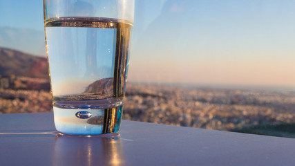 A glass of clean water stands on a table against the backdrop of mountains and sunset.