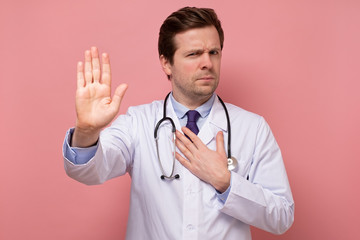 Young handsome man in white coat, intern or doctor showing stop with his hand