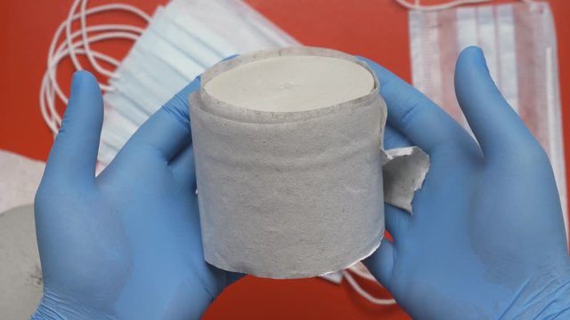 Doctor showing how to use toilet paper to increase antiviral face mask protection. Joke, funny imitation, concept of extra security in pandemic. Human hands protected blue medical gloves. Red backdrop