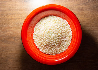 Rice in a red bowl on a wooden background. Top view. Flat lay
