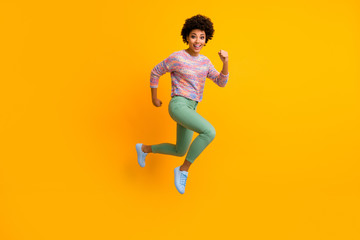 Fototapeta na wymiar Full size photo of crazy dark skin curly lady jumping high rush fast discount shopping black friday low prices wear colorful pullover green pants shoes isolated yellow color background