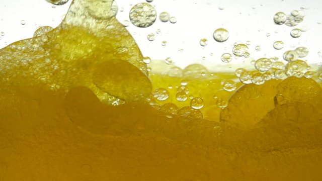 Vegetable black cumin oil mixed with sunflower on white background. Golden hue of liquid oil. Oil is stirred in transparent bowl, bubbles appear, gurgles in water and creates bubble structure of air