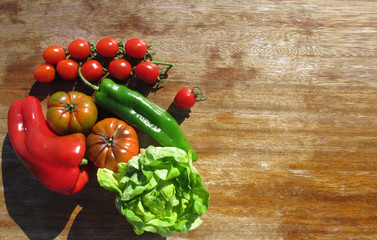 Vegetables illuminated by bright sunlight on an old wooden table. Red and green paprika, tomatoes, tomatoes-cherry,  lettuce. Healthy food. Copy space.