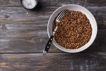 Bowl of boiled red unpolished lentils in a ceramic bowl on a wooden table	