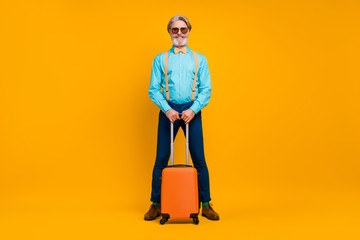 Full size photo of cool grandpa hold rolling suitcase luggage registration table airport wear sun glasses shirt suspenders bow tie pants boots socks isolated yellow color background