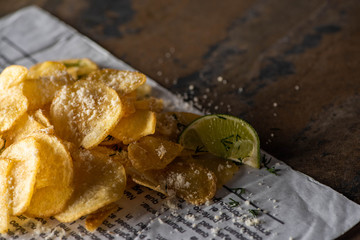 selective focus of crunchy potato chips with salt near sliced lime and newspaper on marble surface