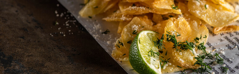 panoramic shot of crunchy potato chips with salt near sliced lime and newspaper on marble surface