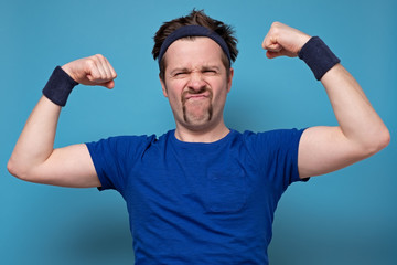 Young handsome funny man wearing holding his arm up to show how strong he is, isolate pink...