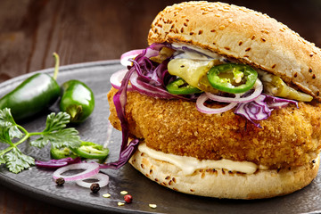 Delicious chicken burger with red onion, pickled cucumber, jalapeno and mayonnaise on a black...