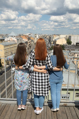 Three girlfriends hugging and watching the city from the roof top