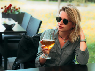 Young woman in sunglasses drinking glass of beer
