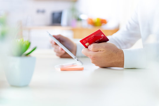 Close up of a caucasian male holding a red credit card in one hand and a tablet computer in the other