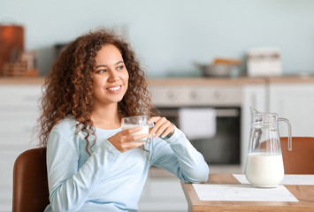 Fototapeta premium Young African-American woman with milk in kitchen