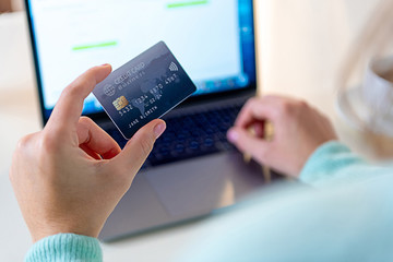Closeup of caucasian left hand, holding a blue credit card and entering data on a laptop