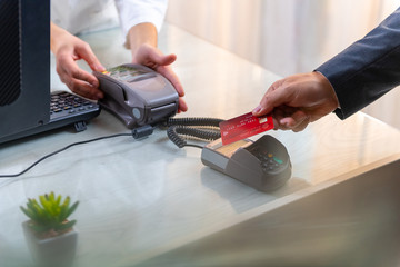 Closeup of caucasian right hand, holding a red credit card on PIN PED while female hands entering amount in POS terminal