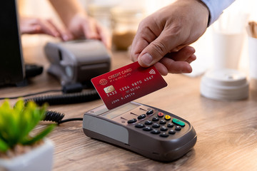 Closeup of caucasian right hand, holding a red credit card and paying a coffee in a coffee shop at a POS terminal
