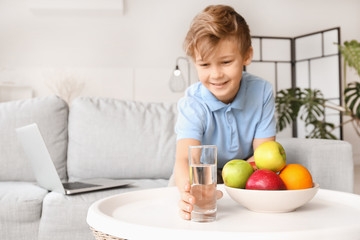 Cute little boy taking glass of water from table at home