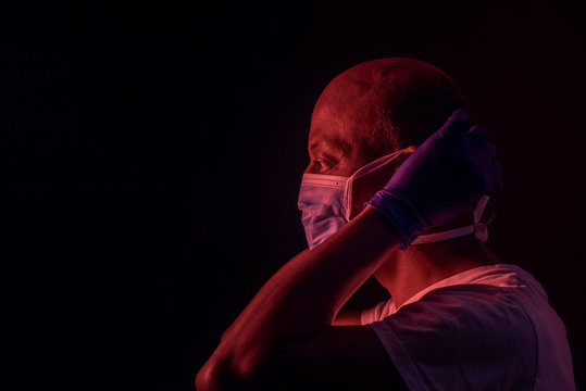 Coronavirus, side portrait of african american man putting on a protective mask. COVID-19 concept. Studio shot with red light on dark background with copyspace