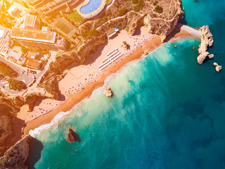 View of stunning turquoise beach, hotel, houses, a pool and tennis field on top of golden color rocks, Algarve, Portugal. 
