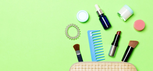Aerial view of a leather cosmetics bag with make up beauty products spilling out on green background. Beautiful skin concept with copy space