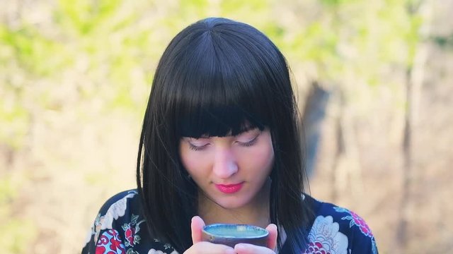 Closeup of young happy woman face with black asian hair drinking and enjoying in teacup cup Japanese sencha or matcha green tea outdoors outside in home backyard garden deck