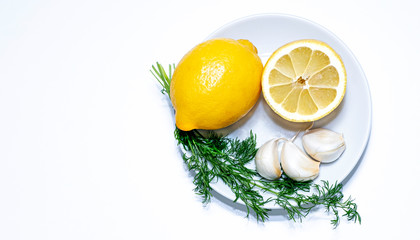 Lemon and garlic, dill on a white plate, backstage. White background and place for copy.