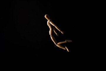 Wooden doll in falling position on black background