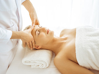 Obraz na płótnie Canvas Beautiful blonde woman enjoying facial massage with closed eyes. Relaxing treatment in medicine and spa center concepts