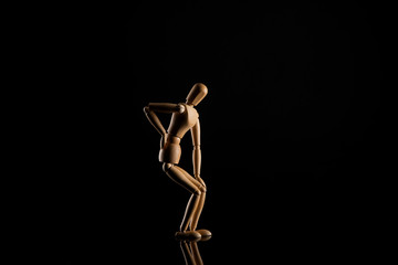 Wooden doll imitating backache on black background