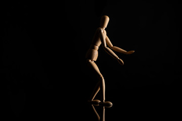 Wooden doll with outstretched hands on black background