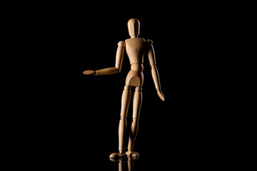 Wooden doll imitating pointing with hand on black background