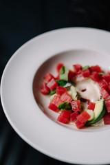 Tuna salad - ceviche with avocado, green basilisk and smoked sauce on a white round plate. Dark background. Top close up view. Smooth image with shallow depth of field.