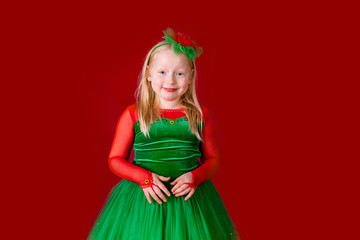 Little blonde girl in a christmas and new year green costume having fun and sending kisses on red background. Space for text. Dreams come true Merry Christmas