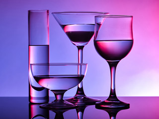 Different glass goblets on a red and purple background. Beautiful still life