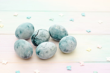Six blue marble eggs, one with crack, painted in hibiscus tea, lie on rainbow background with...