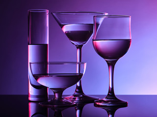 Different glass goblets on a and purple background. Beautiful still life