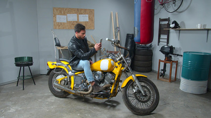 Fototapeta na wymiar Man in leather jacket sits on motorcycle and looks at phone