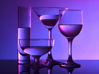 Different glass goblets on a and purple background. Beautiful still life