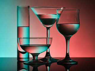 Different glass goblets on a turquoise and orange background. Beautiful still life