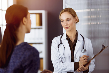 Cheerful smiling female doctor and patient woman discussing current health examination while...