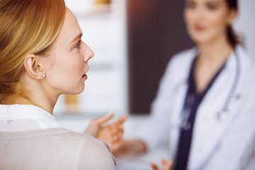 Cheerful smiling female doctor and patient woman discussing current health examination while sitting in sunny clinic. Medicine concept