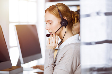 Businesswoman talking by headset in sunny office. Call center and diverse people group in business
