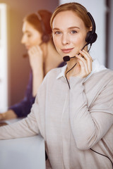 Businesswoman talking by headset in sunny office. Call center and diverse people group in business