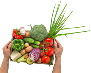 Female hands holding a set of seasonal vegetables in a wooden box on a white background.
